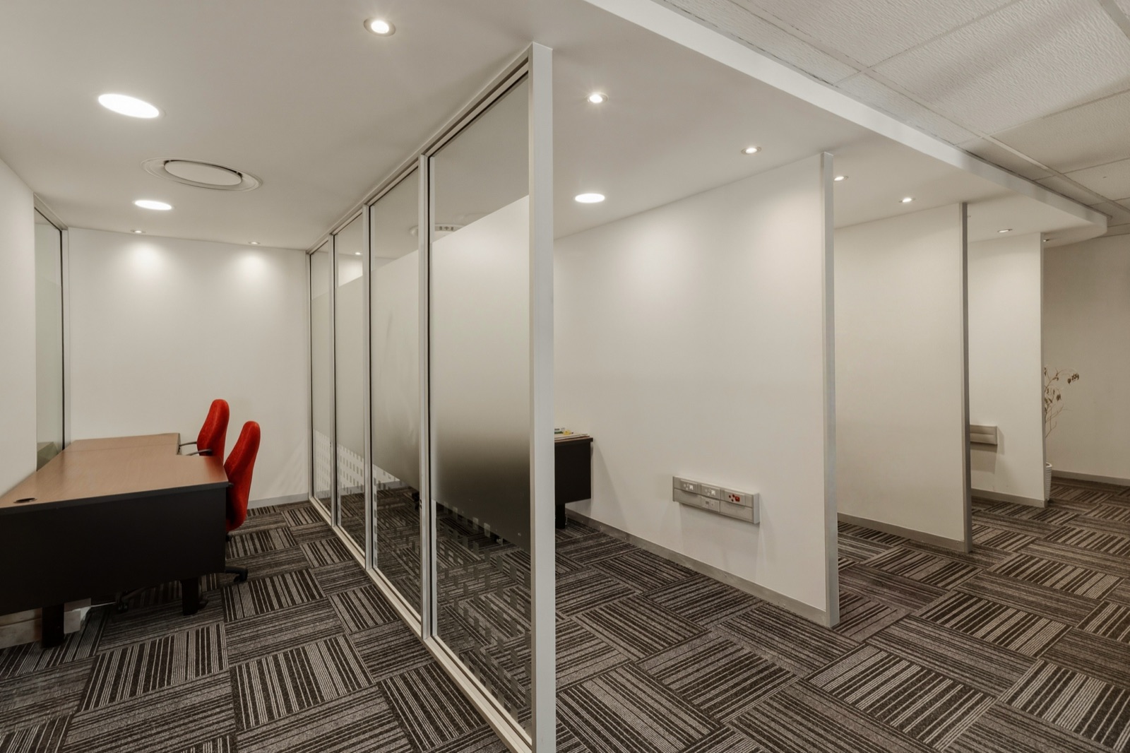 A row of small offices divided by glass and white partitions